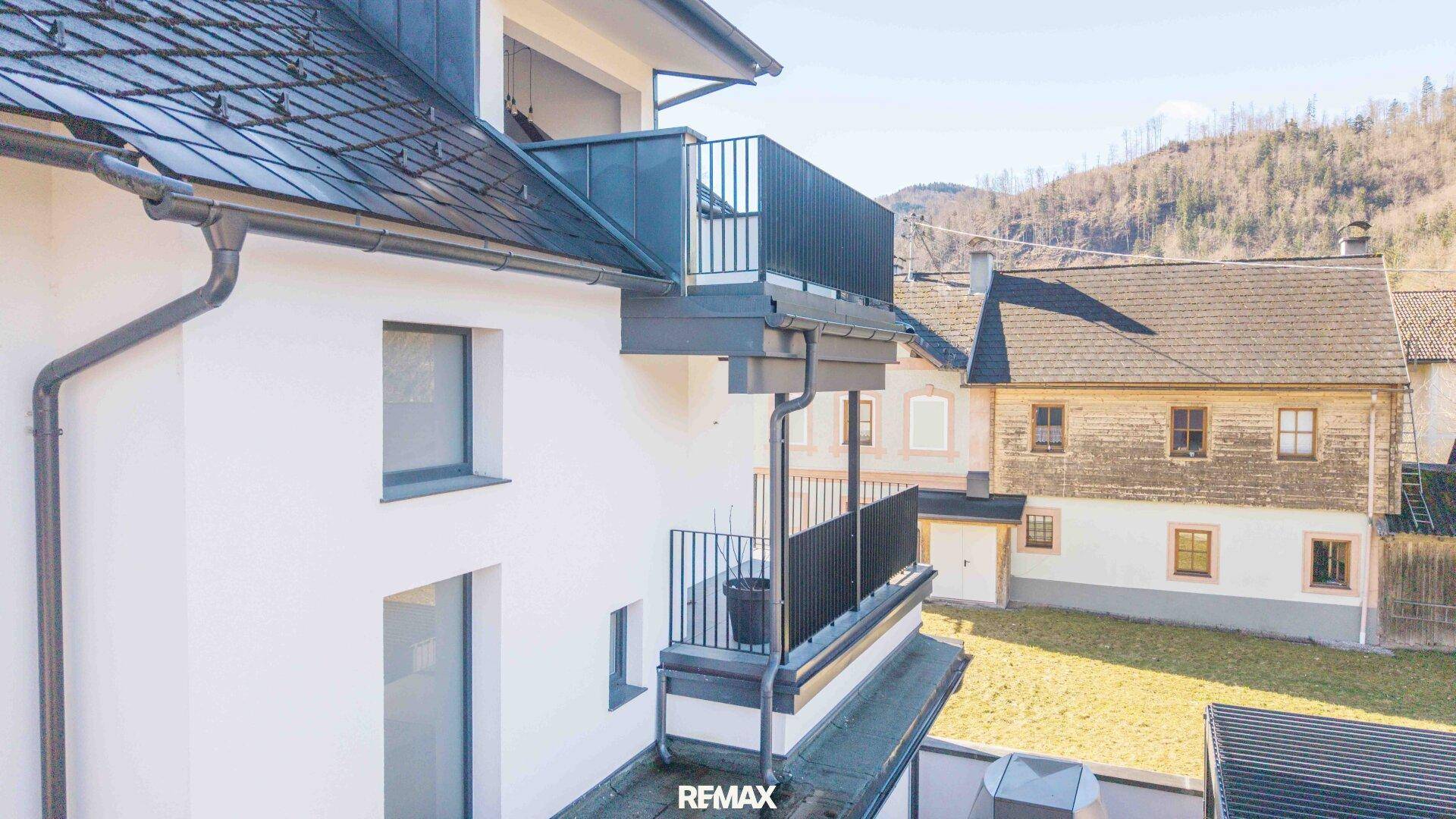 Balkon mit Metallgeländer und Blick auf die umliegenden Häuser und bewaldeten Hügel.