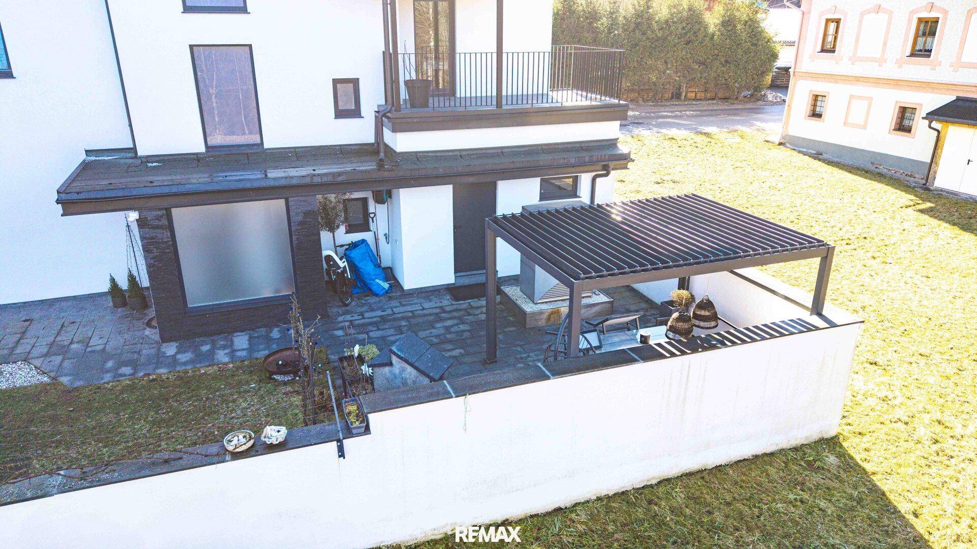 Außenbereich mit Rasenfläche, Terrasse und moderner Pergola für Schatten.
