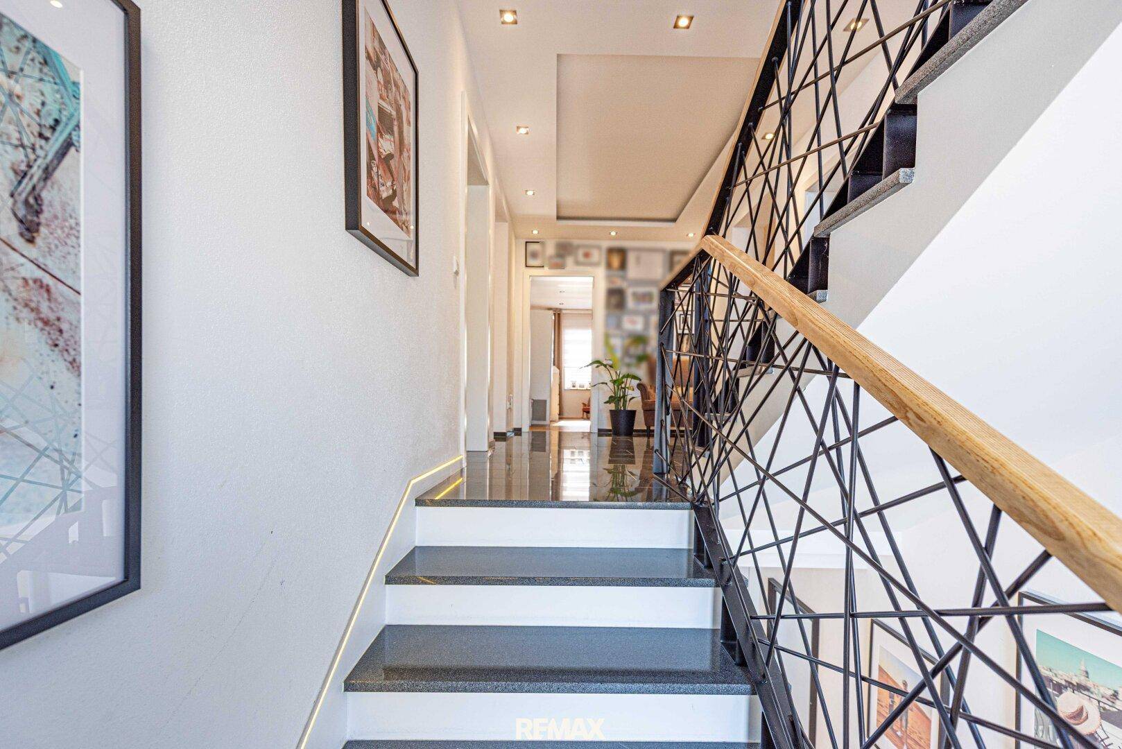 Elegante moderne Treppe mit dunklen Stufen, geometrischem Geländer und Holzhandlauf.