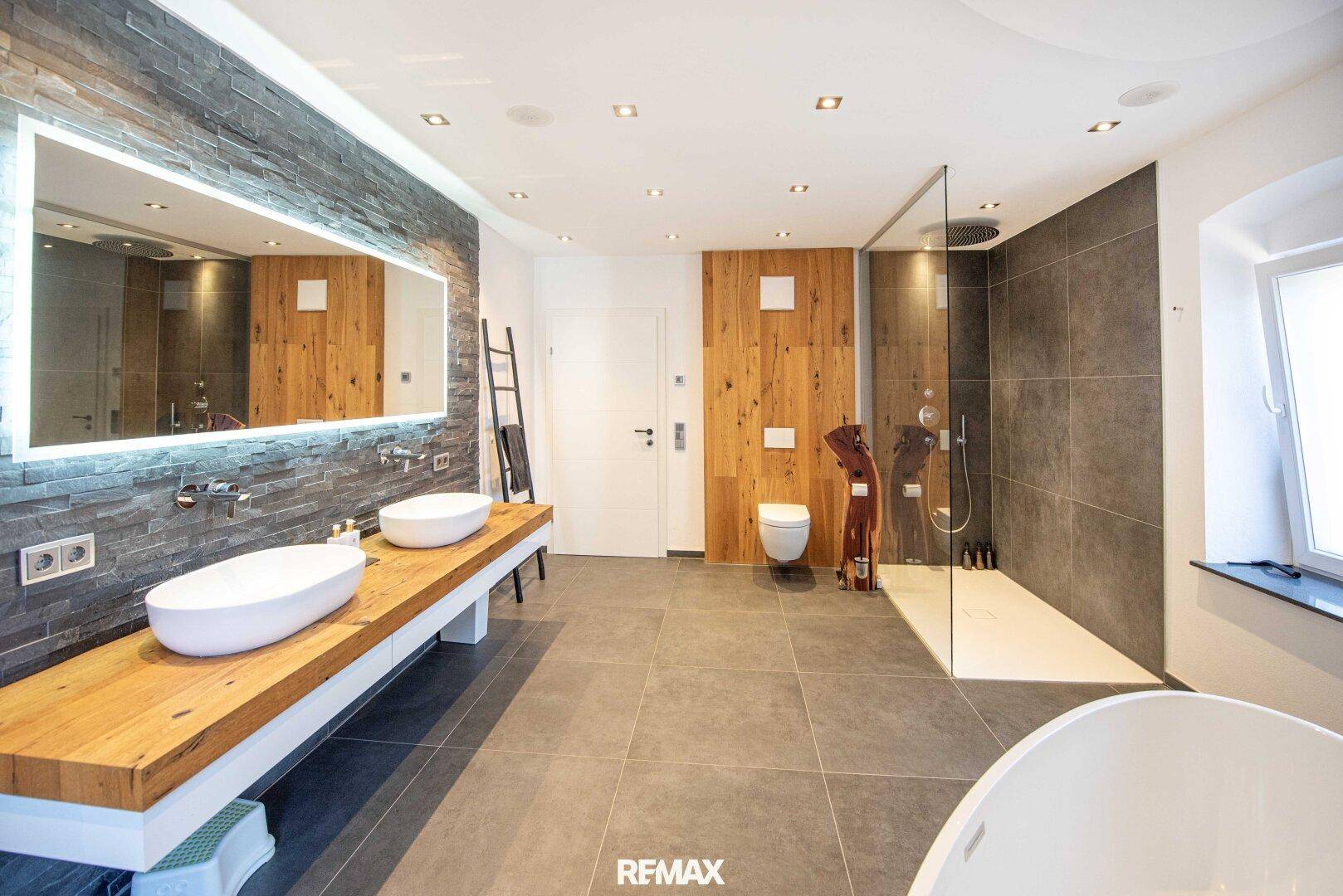Luxuriöses modernes Badezimmer mit Doppelwaschbecken, großer begehbarer Dusche und freistehender Badewanne.