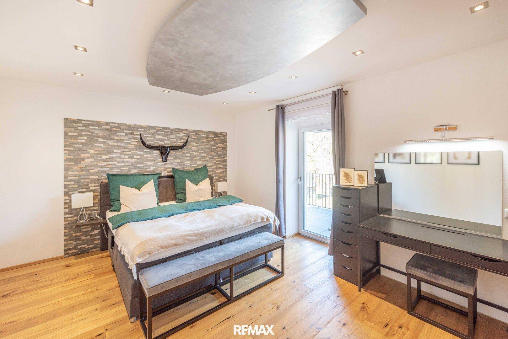 Modernes Schlafzimmer mit Holzboden, Steinwandakzent und Zugang zu einem französischen Balkon.