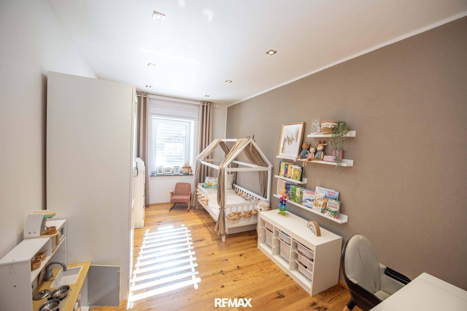 Kinderzimmer mit Holzboden, Spielbett und Regalen für Bücher und Spielzeug.