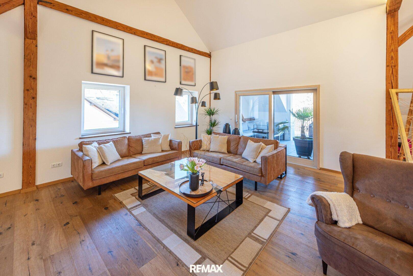 Helles Wohnzimmer mit Holzbalken, Parkettboden und Zugang zu einem Außenbereich.