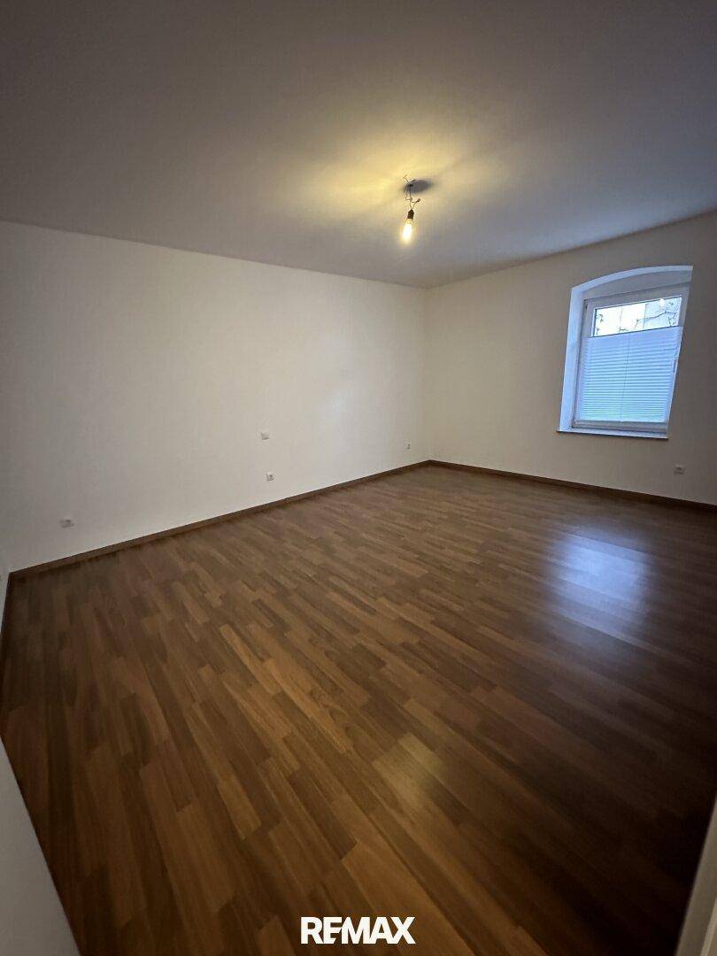 Heller, leerer Raum mit Laminatboden und einem Fenster, ideal als Wohnzimmer.