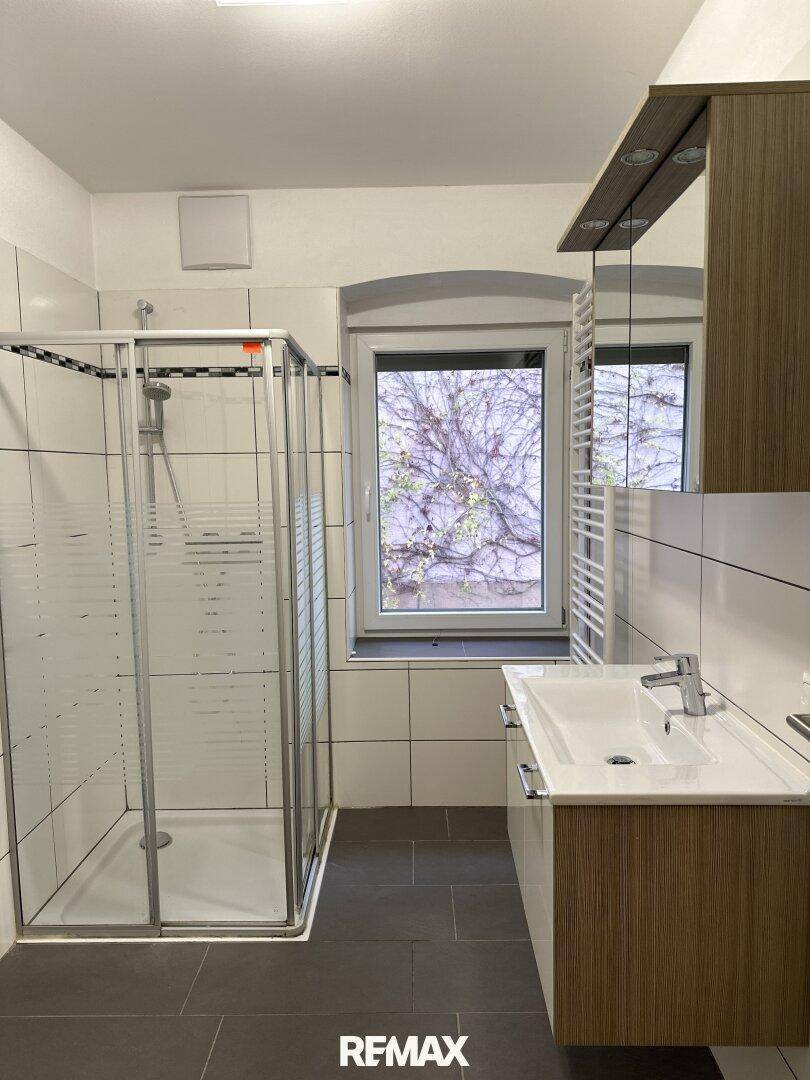 Badezimmer mit Duschkabine, Einzelwaschbecken, Spiegelschrank und beheiztem Handtuchhalter.