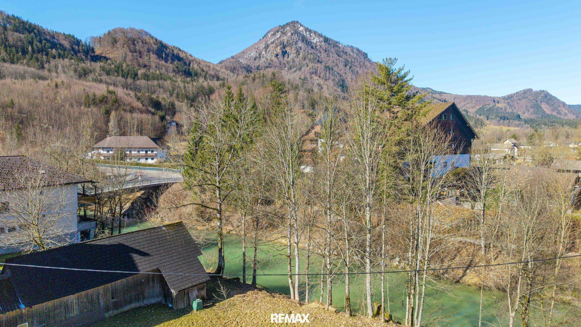 Malerischer Blick auf einen Fluss, bewaldete Hügel und Berge unter blauem Himmel.