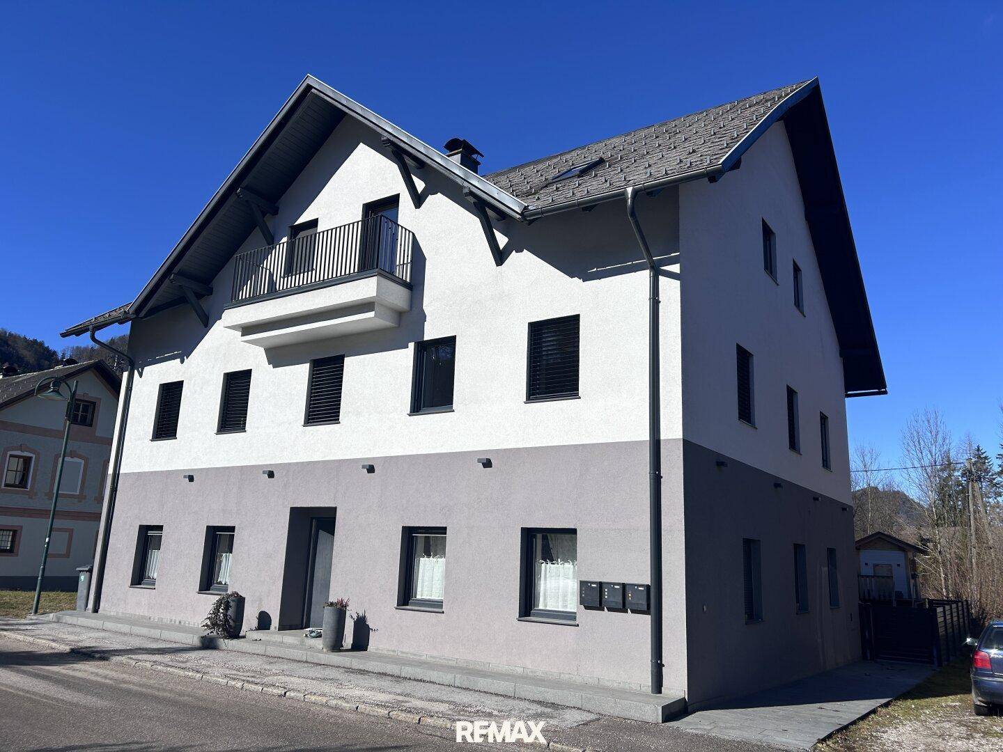 Moderne Gebäudefassade mit zweifarbigem Anstrich, schwarzen Fensterläden und kleinem Balkon.