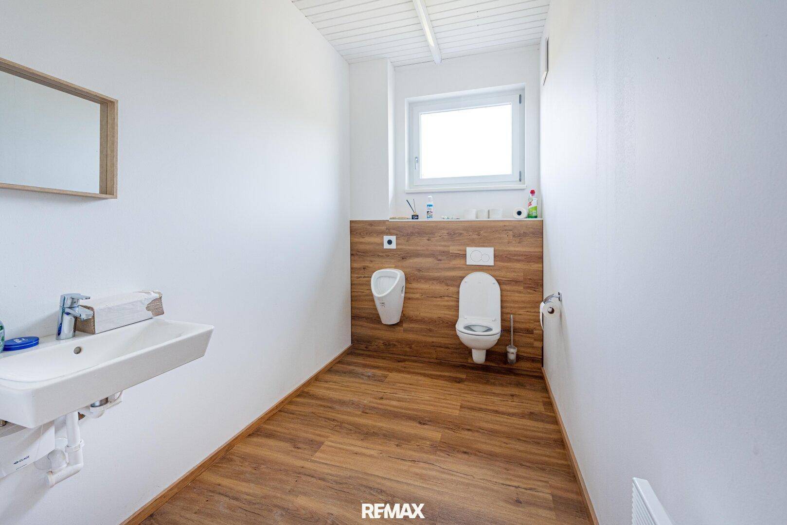 Toilettenraum mit Urinal, WC, Waschbecken und Fenster, ausgestattet mit modernem Laminatboden.