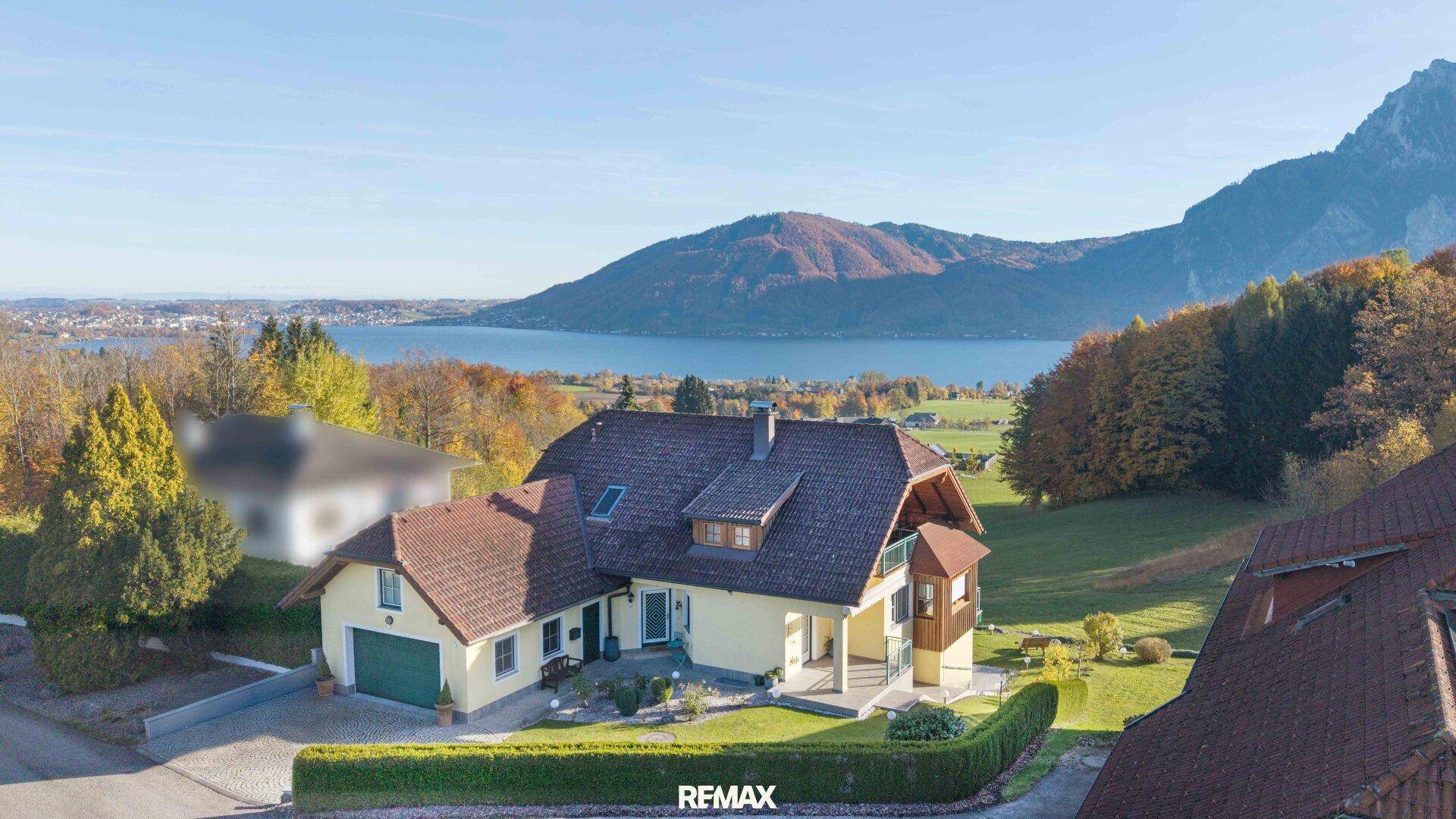 Panoramablick auf ein Haus mit See- und Bergsicht, umgeben von grüner Landschaft und Bäumen.