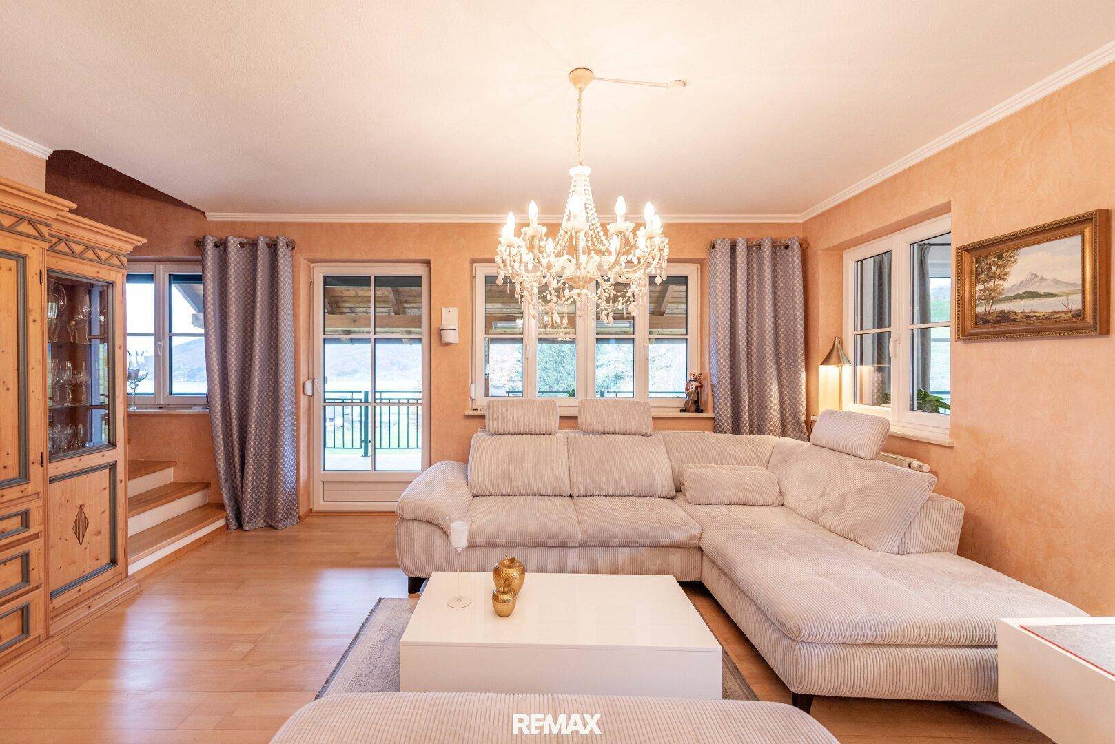 Helles Wohnzimmer mit beigem Sofa, Kronleuchter und Zugang zu einem Balkon oder einer Terrasse.