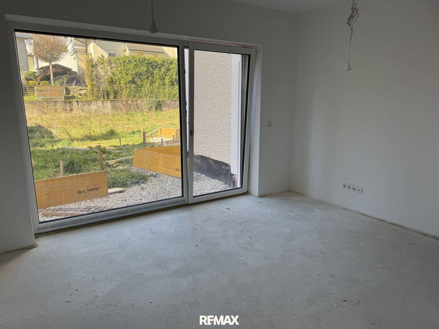 Leerer Raum mit großer Glasschiebetür, die einen Blick auf den Garten freigibt.
