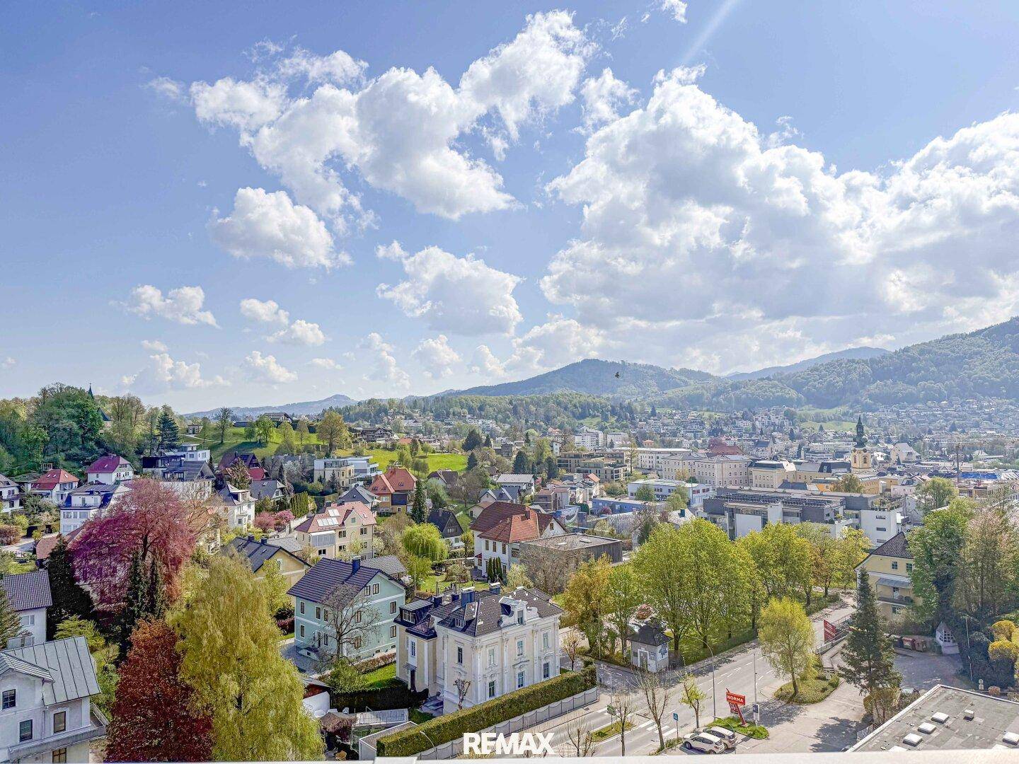Panoramablick über eine charmante Stadt mit vielfältiger Architektur, umgeben von üppigem Grün und majestätischen Bergen.