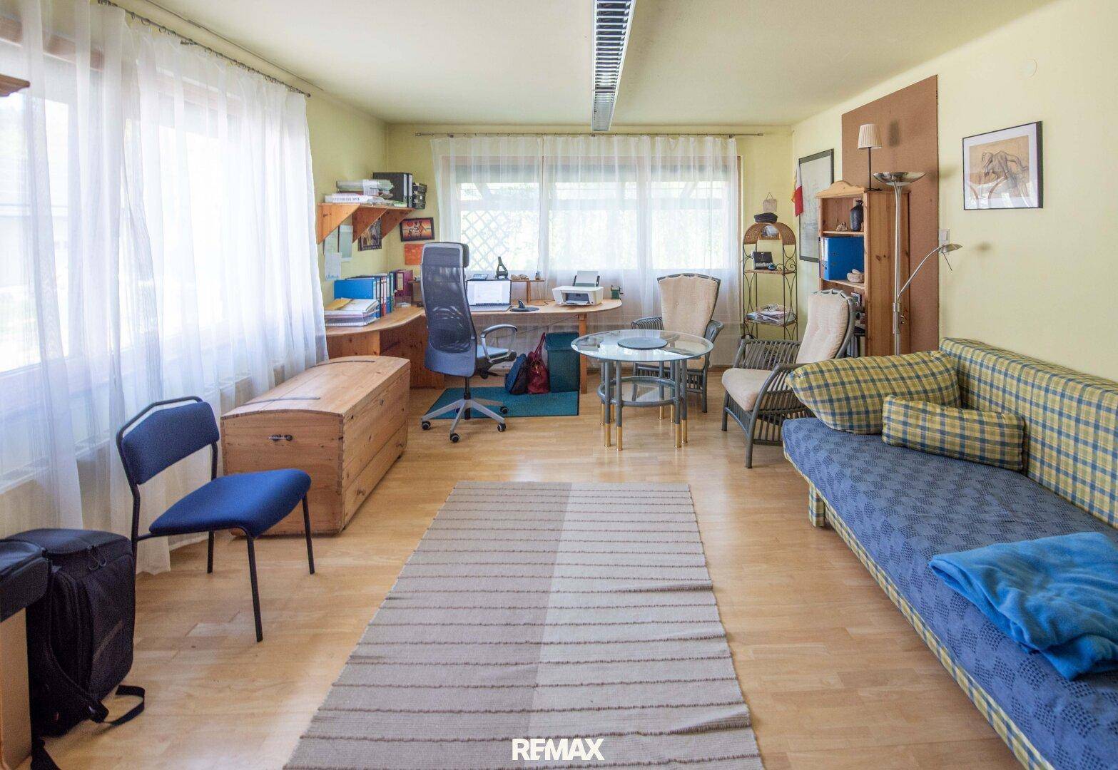 Geräumiges Wohnzimmer mit hellem Holzboden, Sofa und einem integrierten Arbeitsbereich.