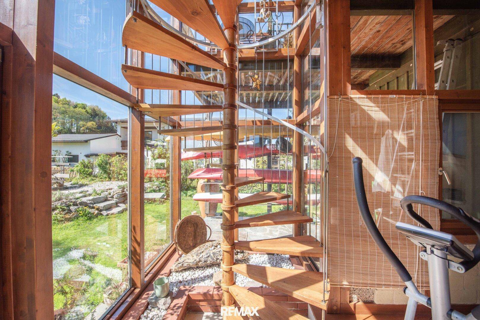 Elegante Holz-Wendeltreppe in einem lichtdurchfluteten Bereich mit großen Glasfenstern.