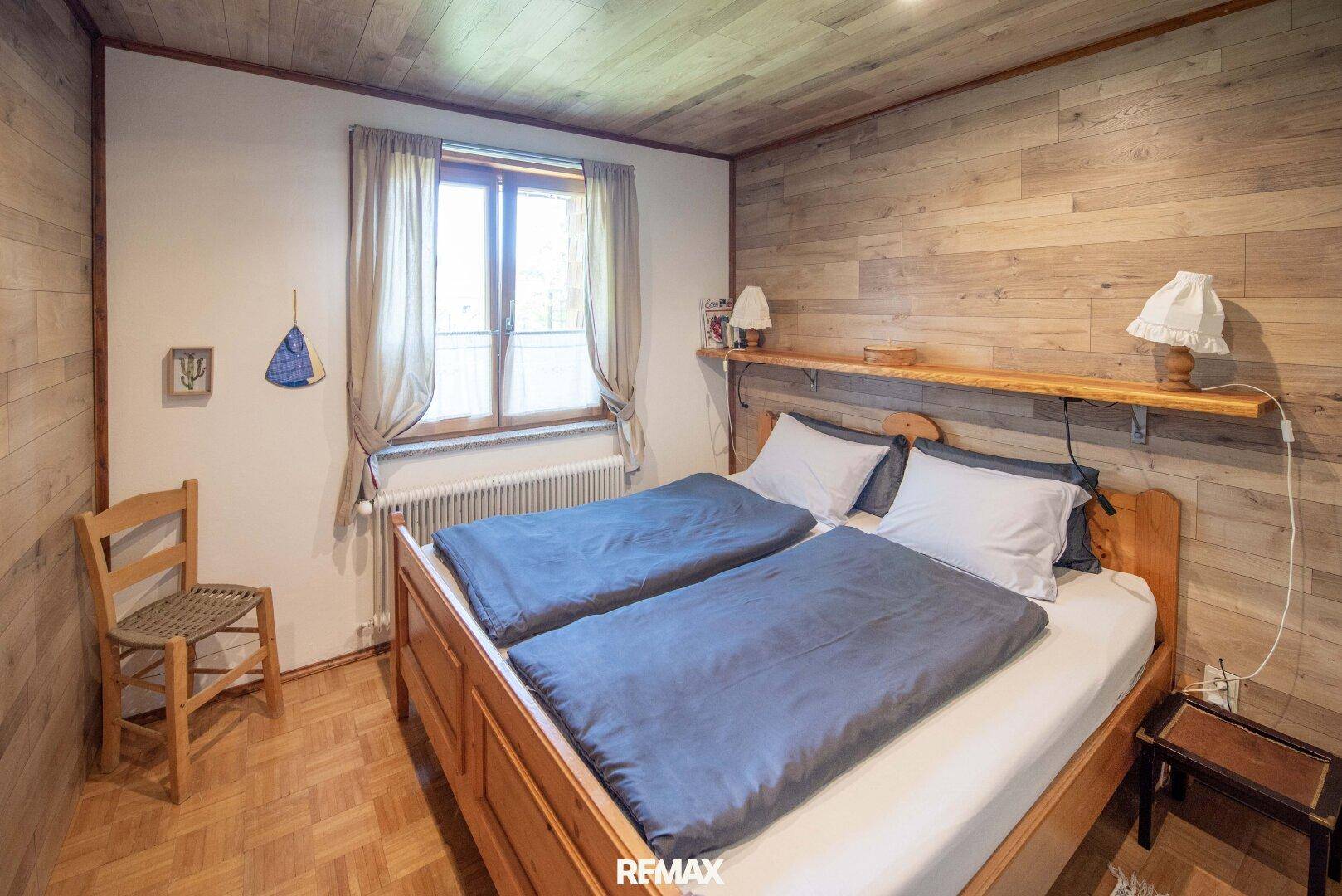 Gemütliches Schlafzimmer mit Holzwänden, Parkettboden und einem Doppelbett.