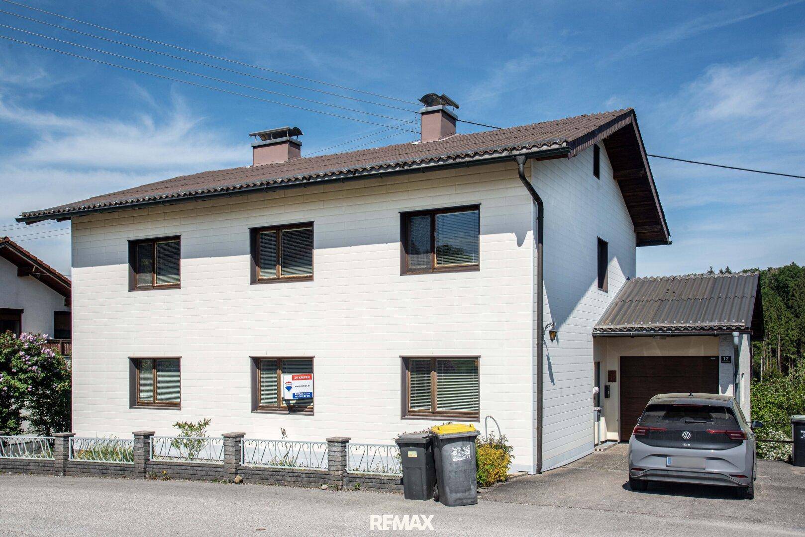 Vorderansicht des Hauses mit weißer Fassade, Satteldach und integrierter Garage.