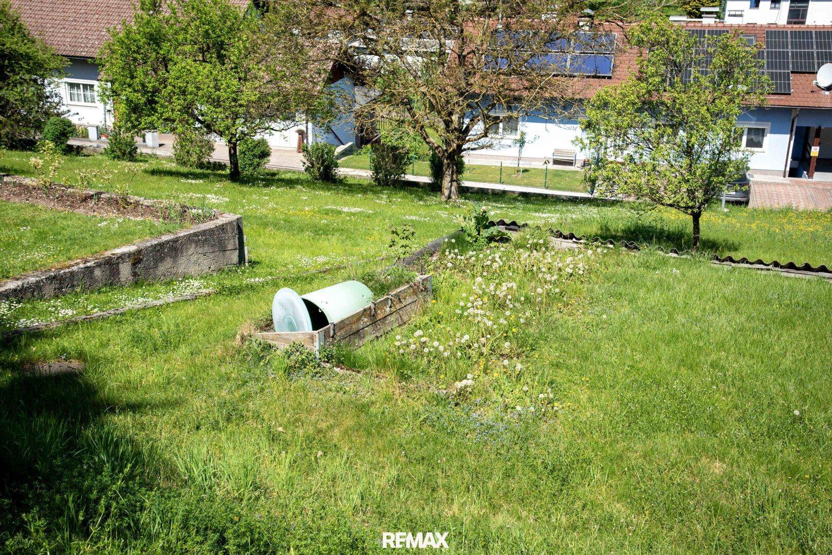 Gartenbereich mit Rasenfläche, Betonbegrenzungen und einem grünen Tank im Freien.
