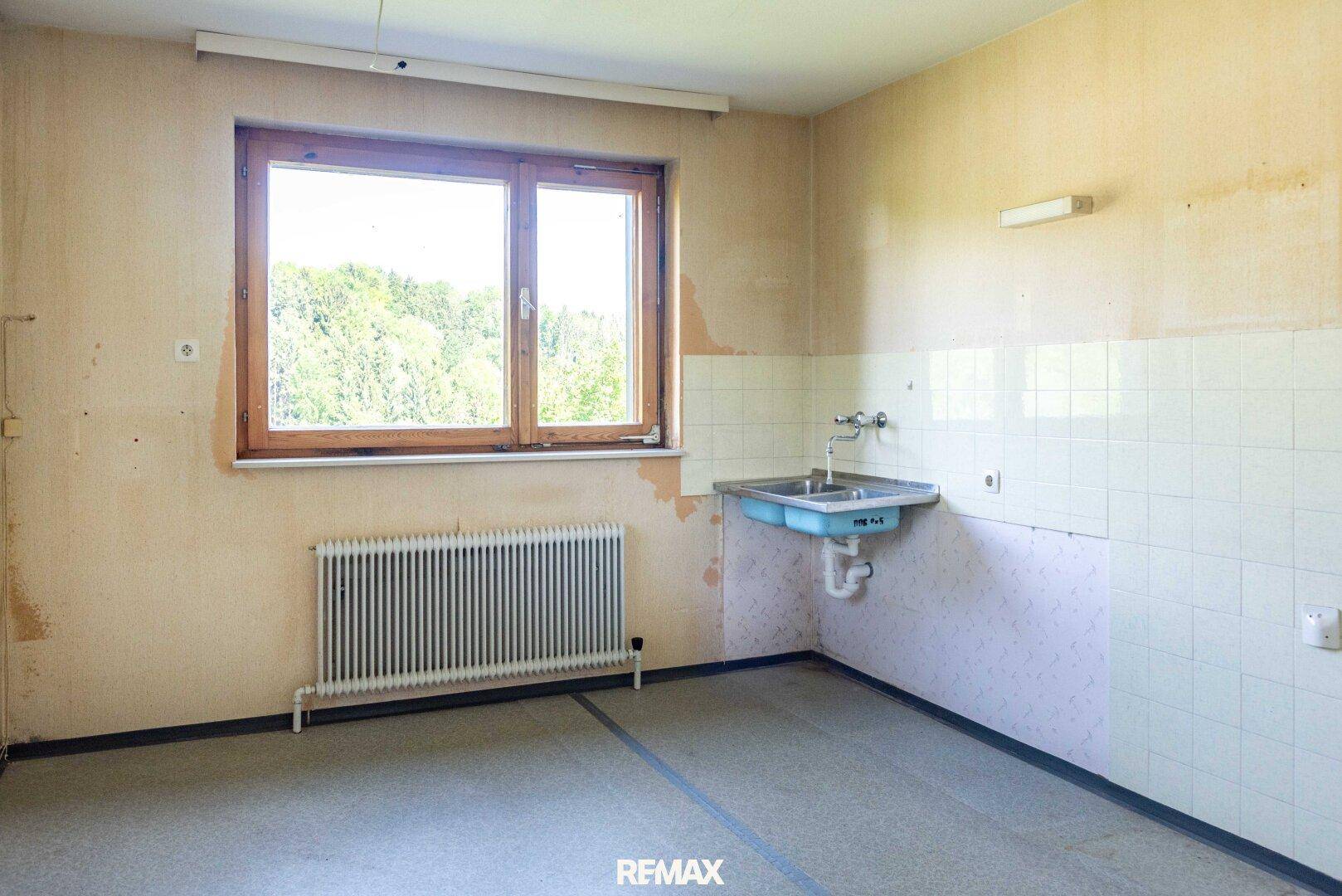 Leerer Raum mit Fenster, Heizkörper und einfachem Waschbecken, renovierungsbedürftig.