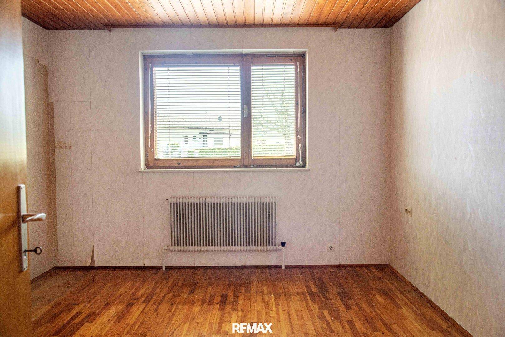 Schlafzimmer mit Holzboden, Holzdecke und Fenster mit Jalousien.