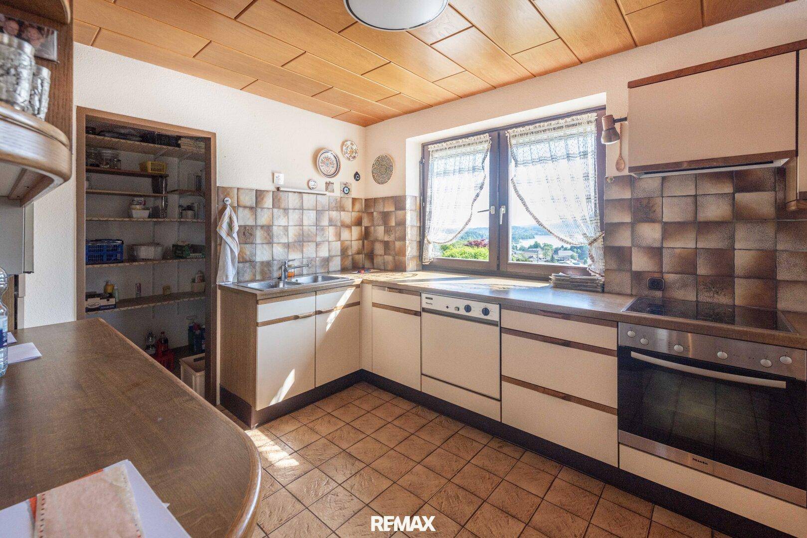 Funktionale Küche mit Fliesenboden, Holzdecke, Einbauschränken und Zugang zu einer Speisekammer.