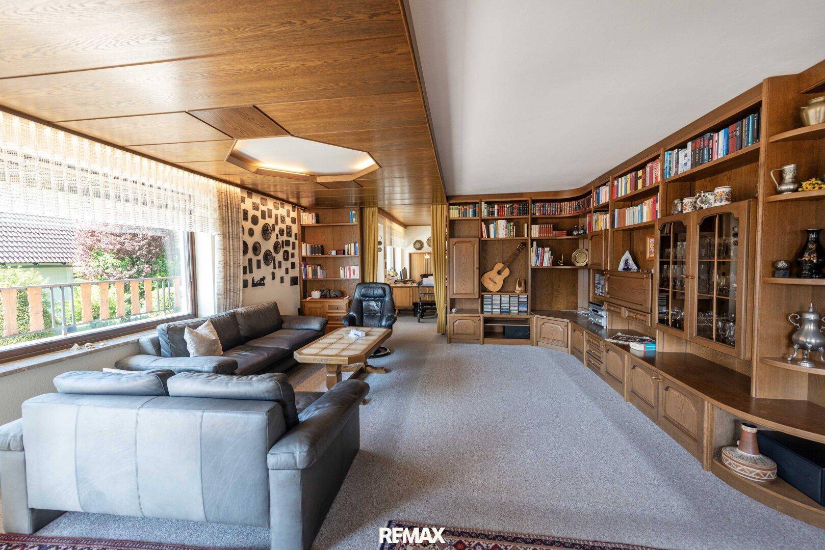Geräumiges Wohnzimmer mit umfangreichen Holzregalen, gemütlicher Sitzecke und Holztäfelung an der Decke.