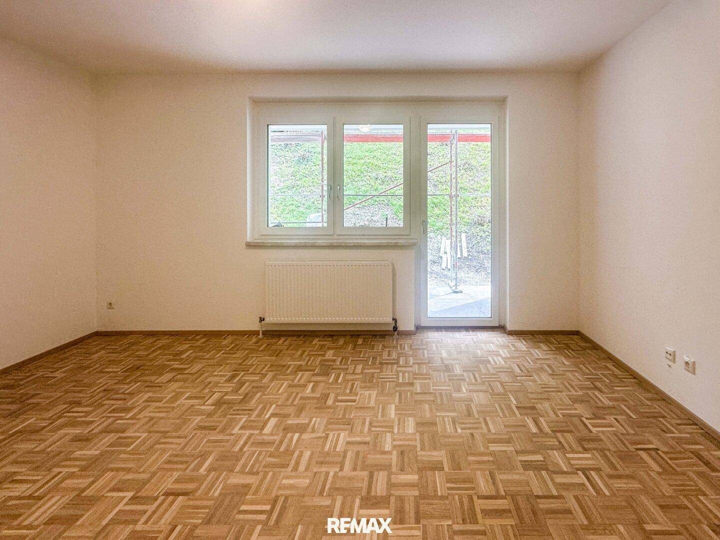 Geräumiges, helles Zimmer mit Parkettboden, großen Fenstern und Zugang zum Außenbereich.