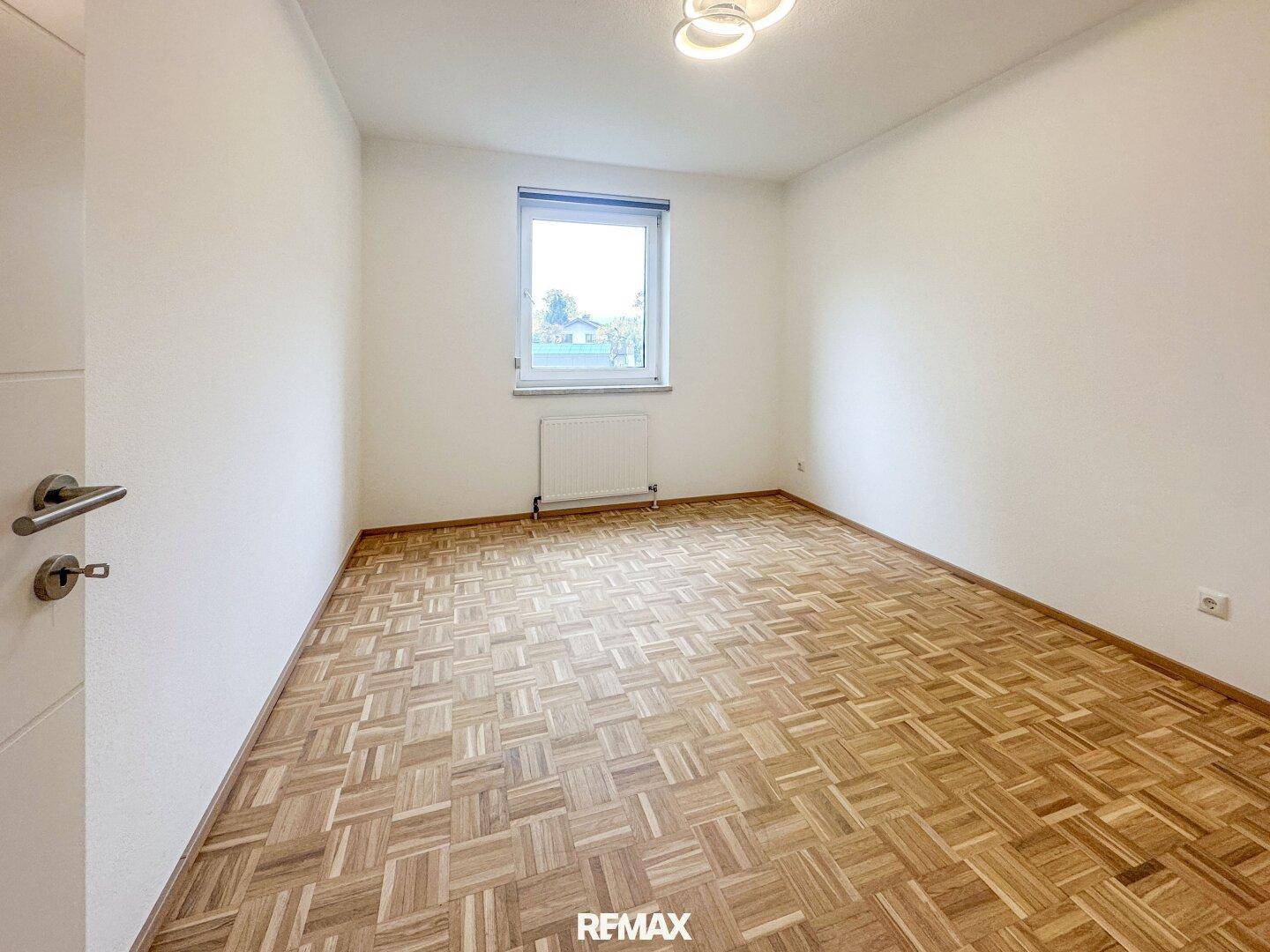 Ruhiges Schlafzimmer mit Parkettboden, weiß gestrichenen Wänden und einem Fenster.