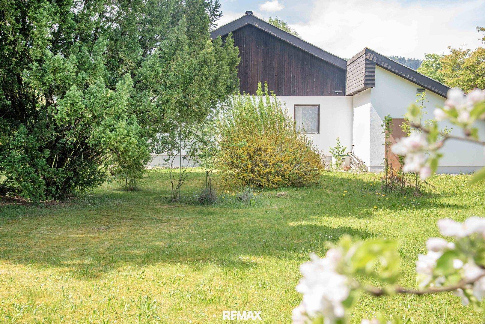 Großer grüner Gartenbereich mit Rasenfläche, Bäumen und Sträuchern, umgeben von Natur.