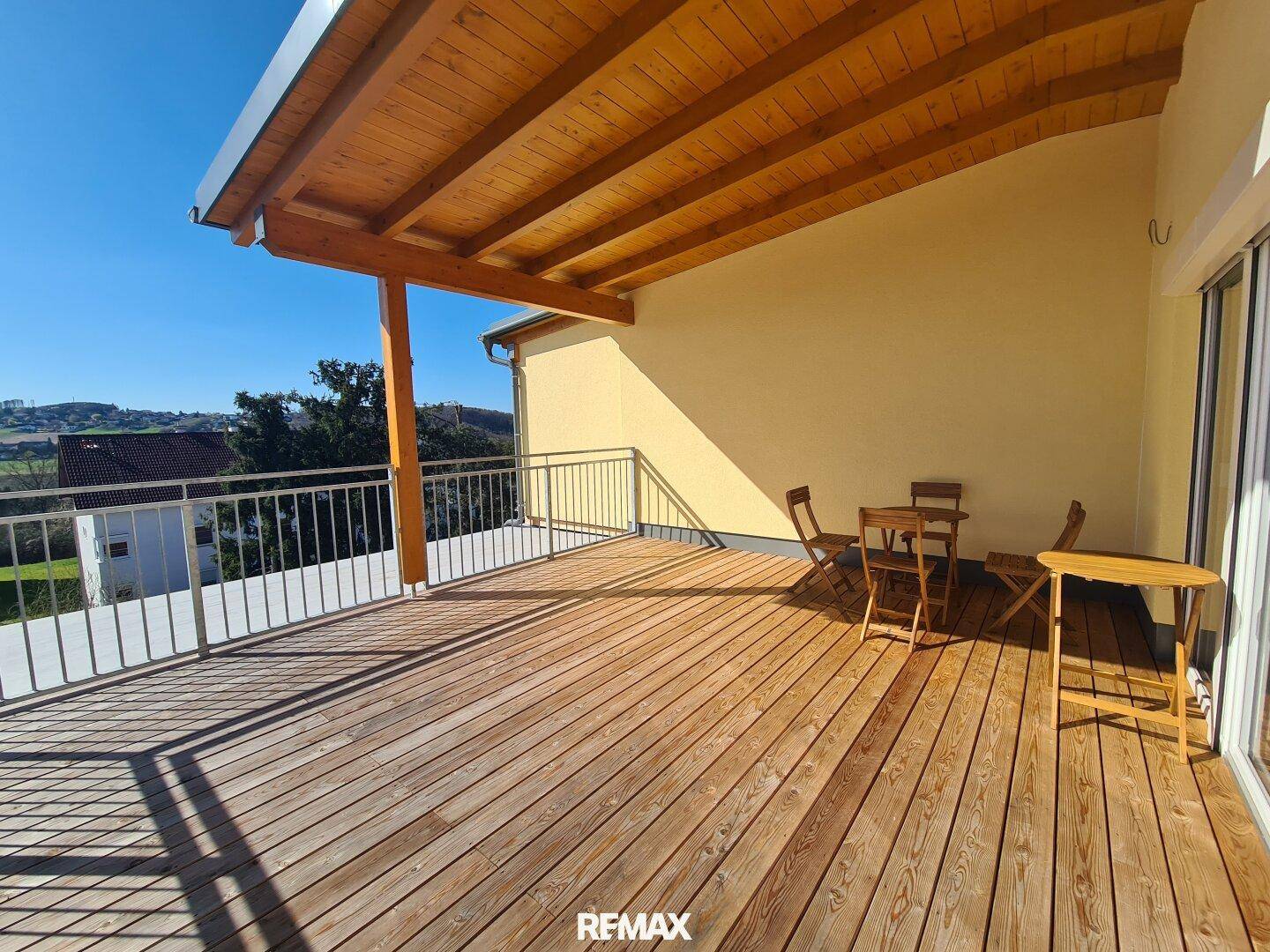 Weitläufige Holzterrasse mit schützendem Holzdach und Blick auf die umliegende Landschaft und Berge.