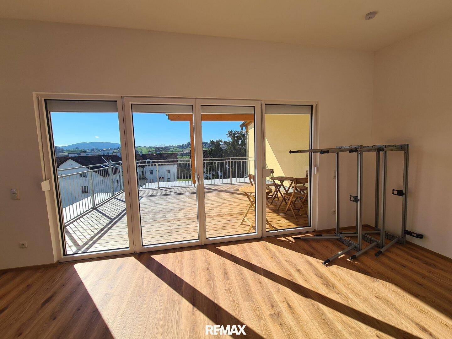 Heller Wohnraum mit großen Glasschiebetüren, die auf die sonnige Holzterrasse mit Bergblick führen.