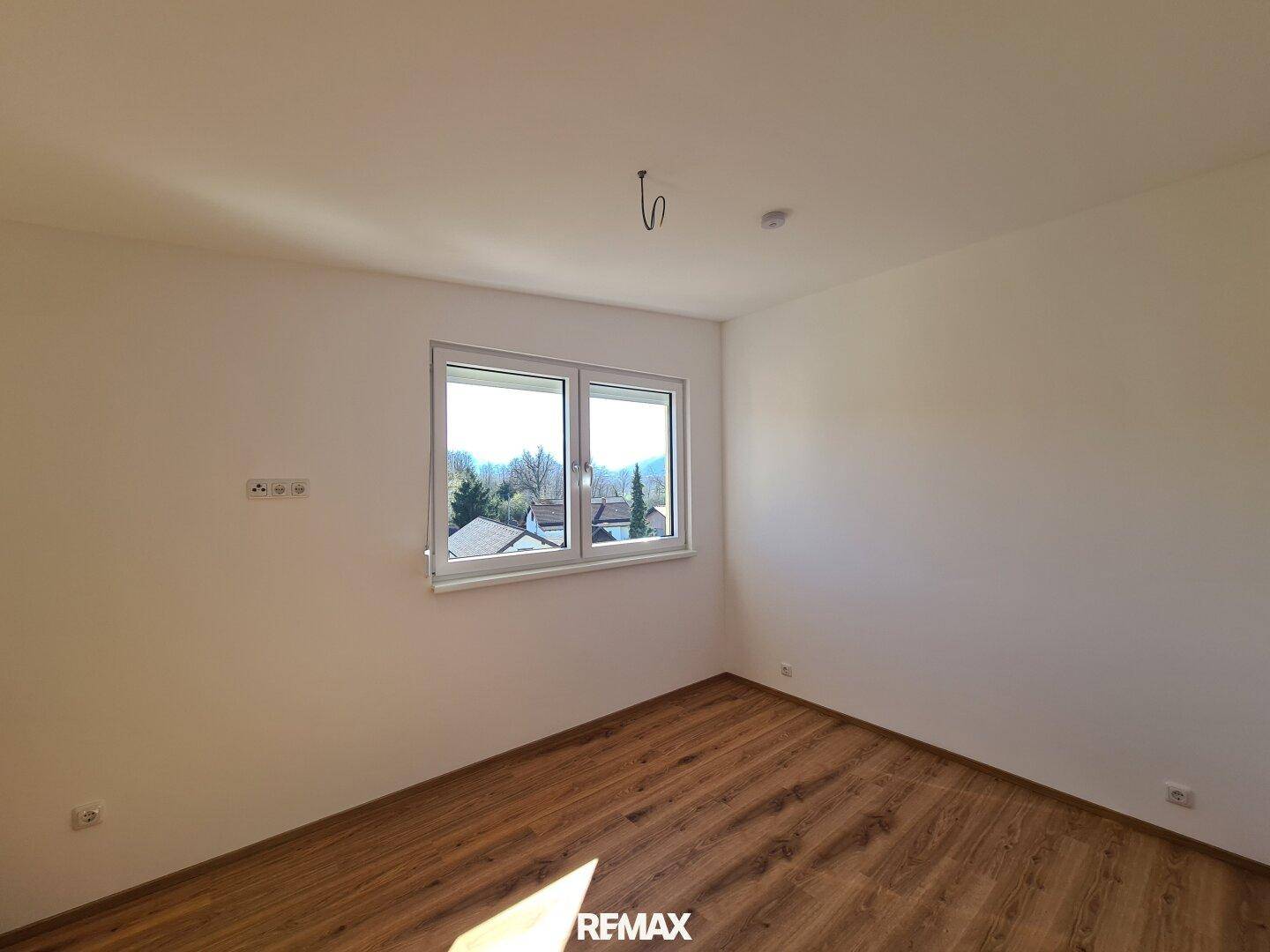 Helles Schlafzimmer mit Laminatboden und einem Fenster, das viel Tageslicht in den Raum lässt.