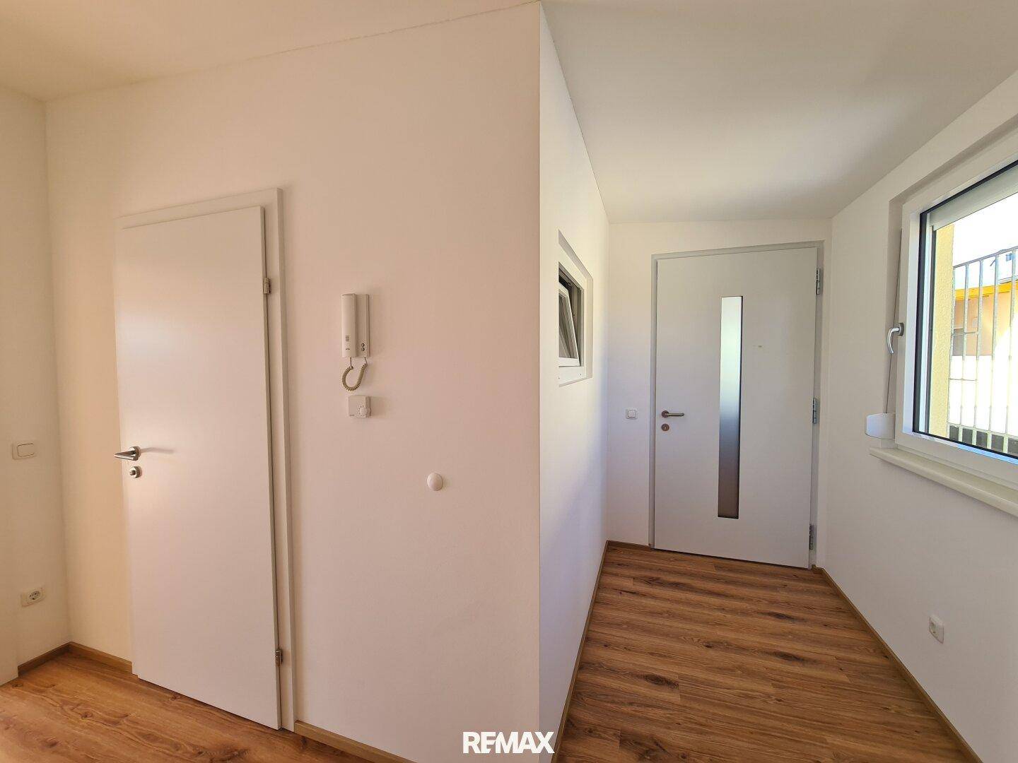 Heller Flur mit Laminatboden, weißen Türen und einem Fenster, das den Eingangsbereich erhellt.