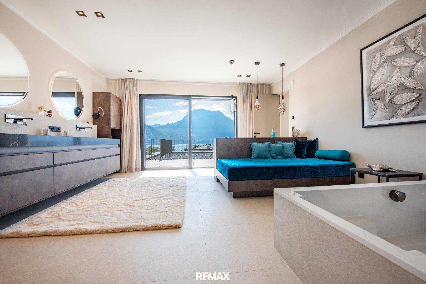 Luxuriöses Badezimmer mit Doppelwaschbecken, freistehender Badewanne und Seeblick vom Balkon.