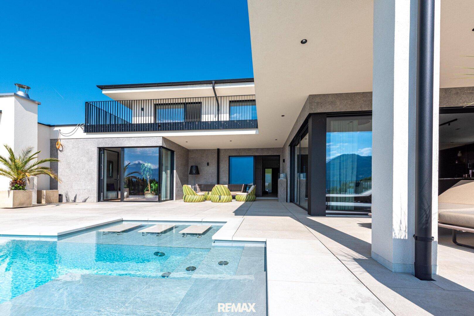 Moderne Villa mit großzügiger Poolterrasse, Sitzgelegenheiten und direktem Zugang zum Innenbereich.