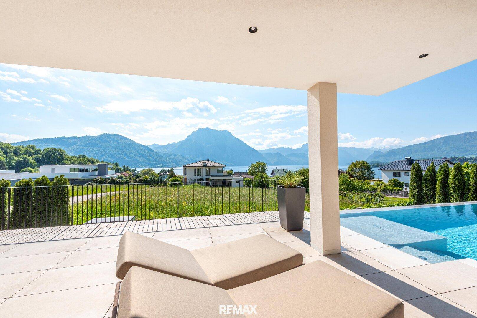 Überdachte Terrasse mit bequemen Liegen, Infinity-Pool und weitem Blick auf den See.