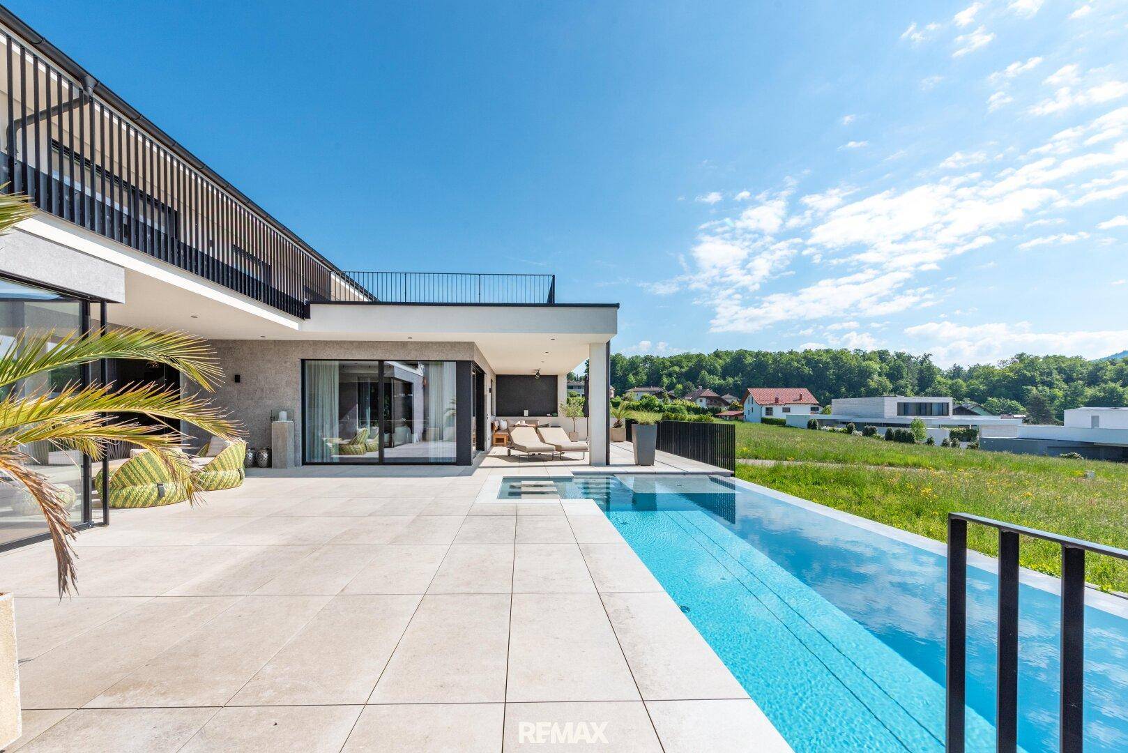 Moderne Architektur mit weitläufiger Terrasse und Infinity-Pool, umgeben von grüner Landschaft.