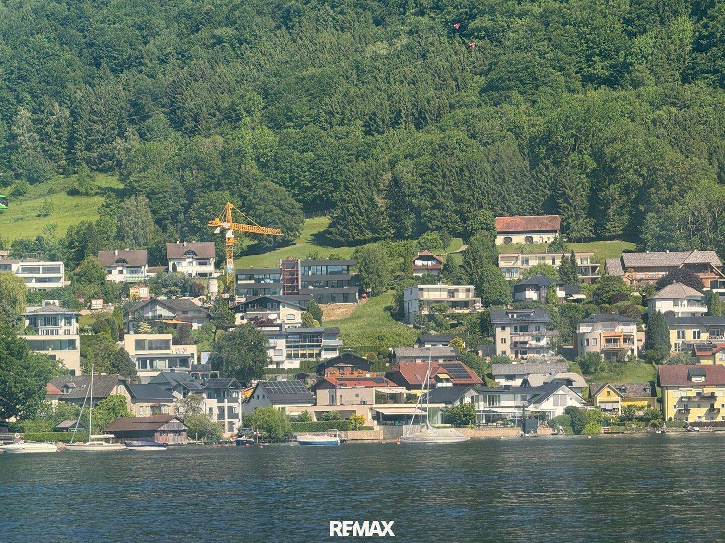 Malerische Ansicht eines Dorfes am Seeufer mit Häusern am Hang und üppiger grüner Vegetation.