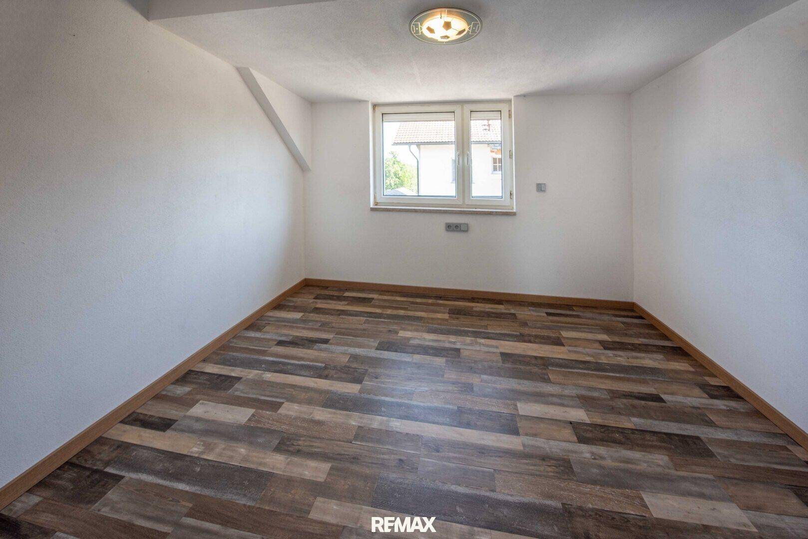 Heller Raum mit Laminatboden und weiß gestrichenen Wänden, gut belichtet durch ein Fenster.