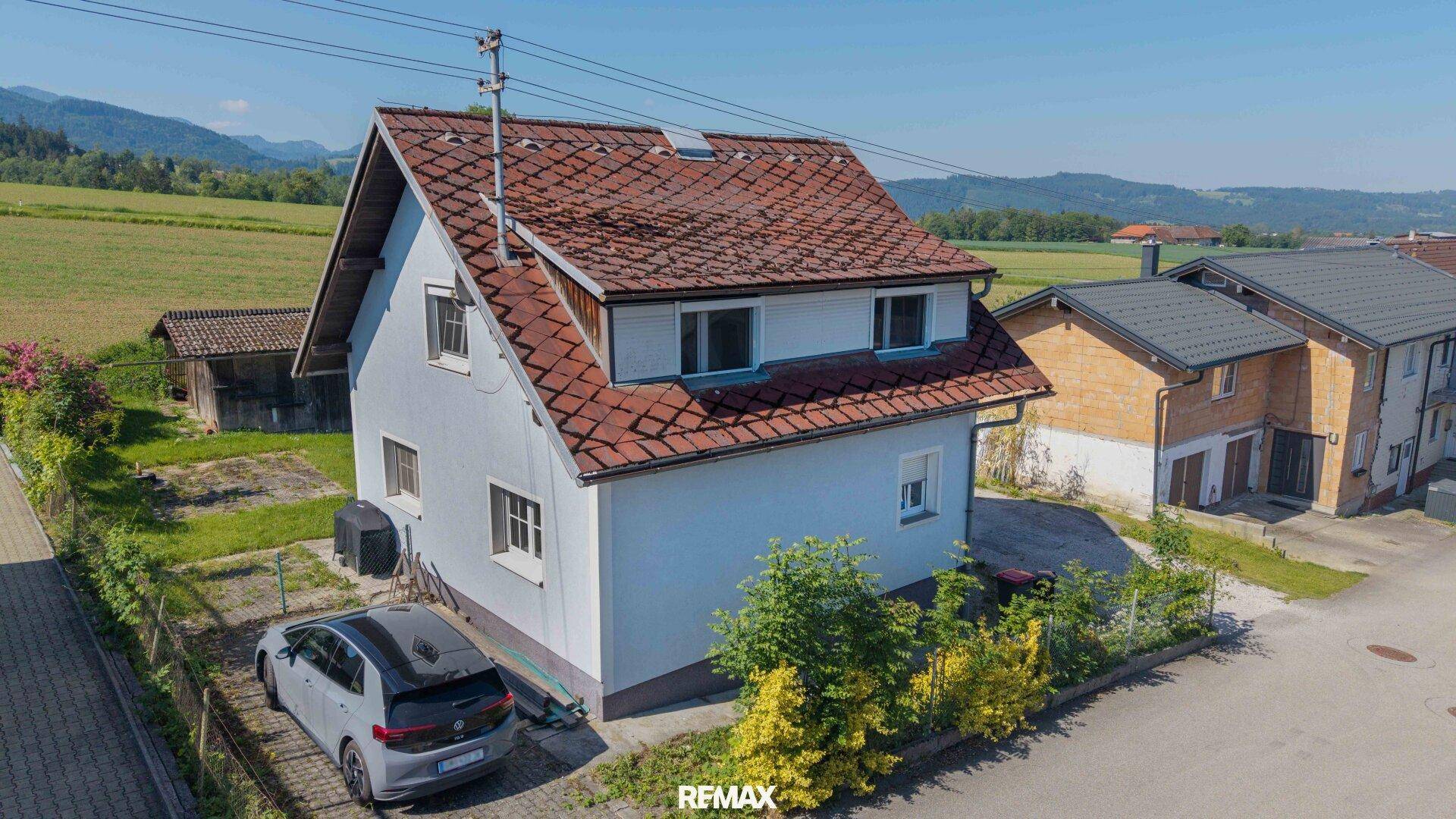Luftaufnahme eines Einfamilienhauses mit rotem Ziegeldach, einem Auto und Gartenbereich in ländlicher Umgebung.