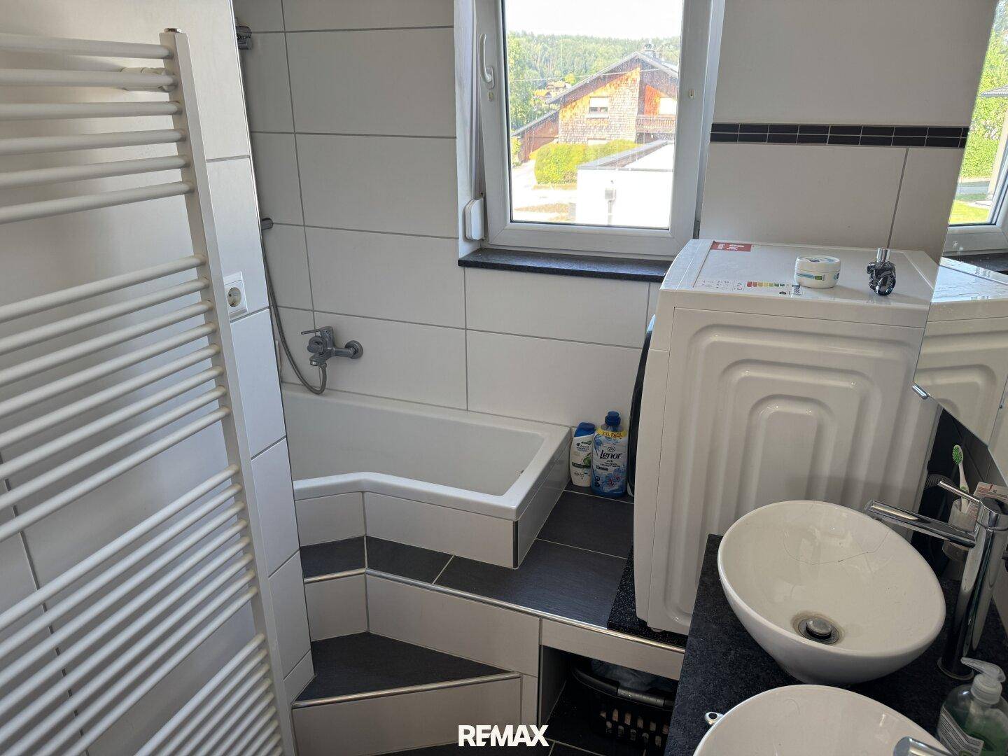 Modernes Badezimmer mit Badewanne, Waschbecken und Waschmaschine, hell gefliest.