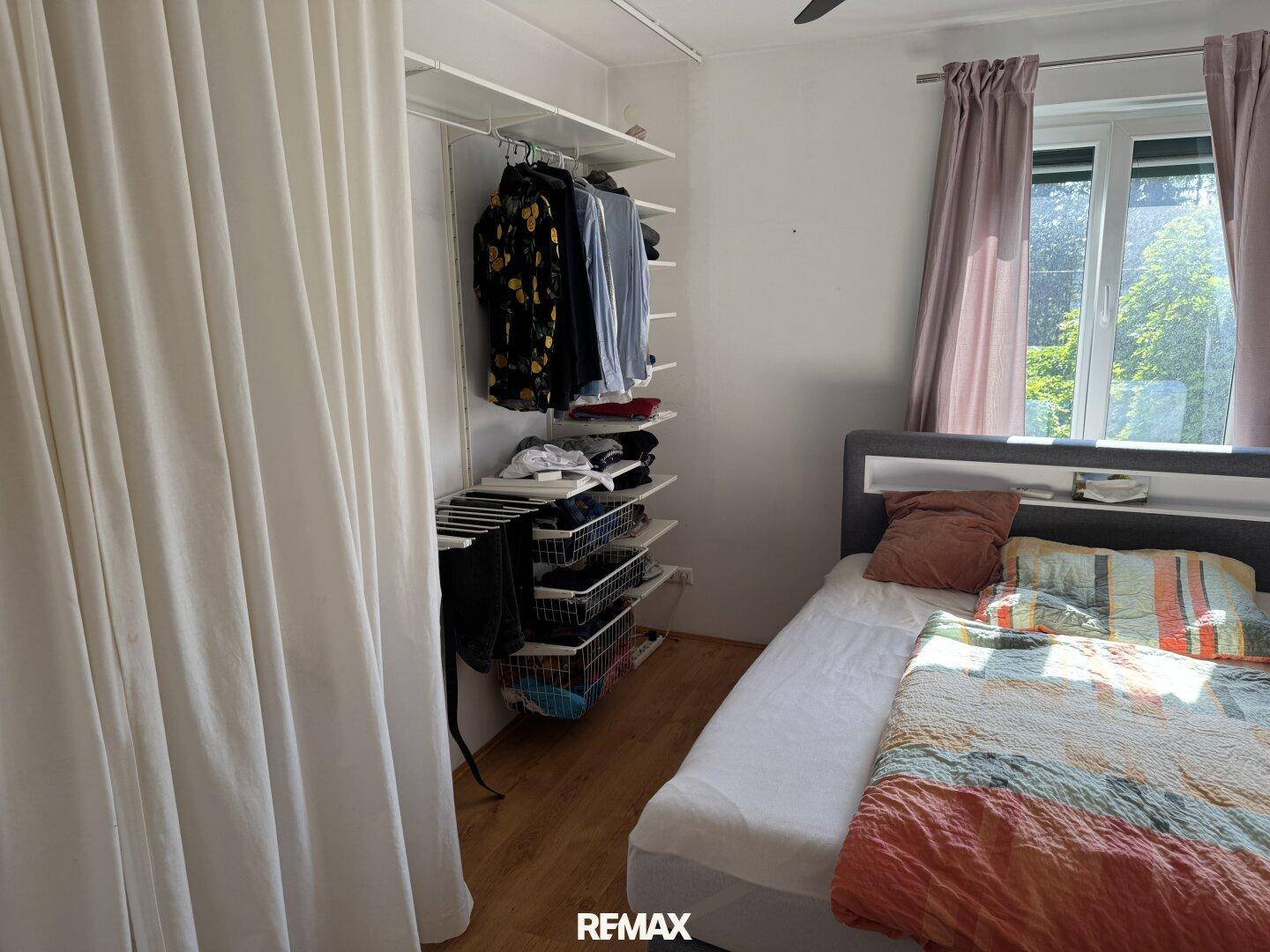 Schlafzimmer mit Holzboden, großem Fenster und offenem Kleiderschrankbereich.