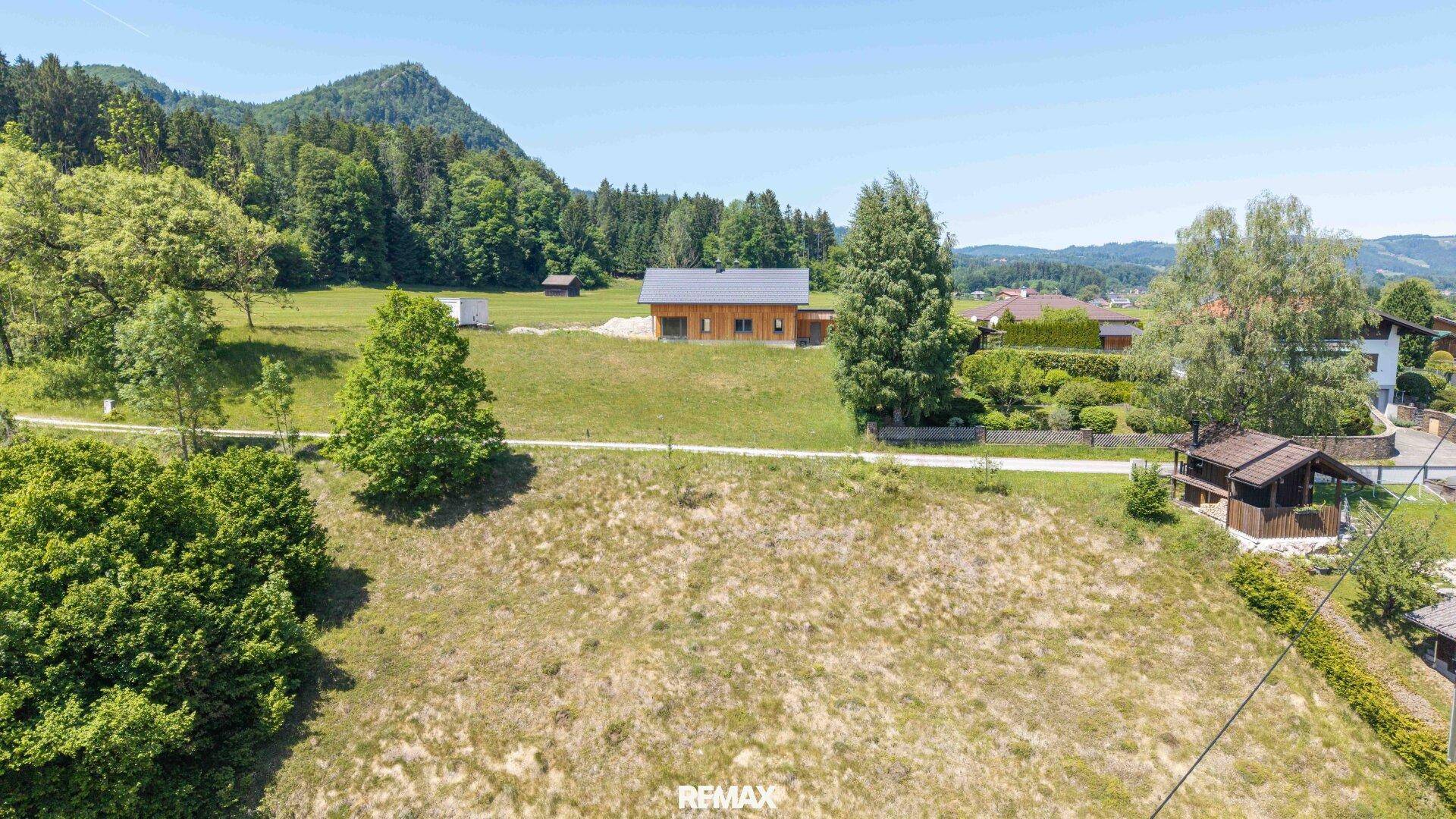 Luftaufnahme eines modernen Holzhauses in ländlicher Umgebung mit Bergblick und viel Grün.