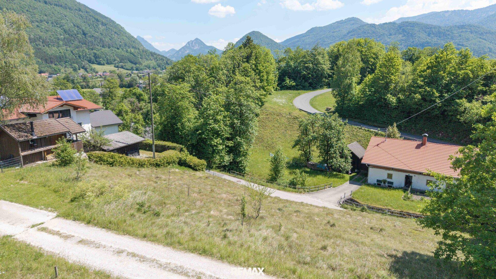 Ländliches Haus in grüner Umgebung mit Bergen im Hintergrund und viel Natur.