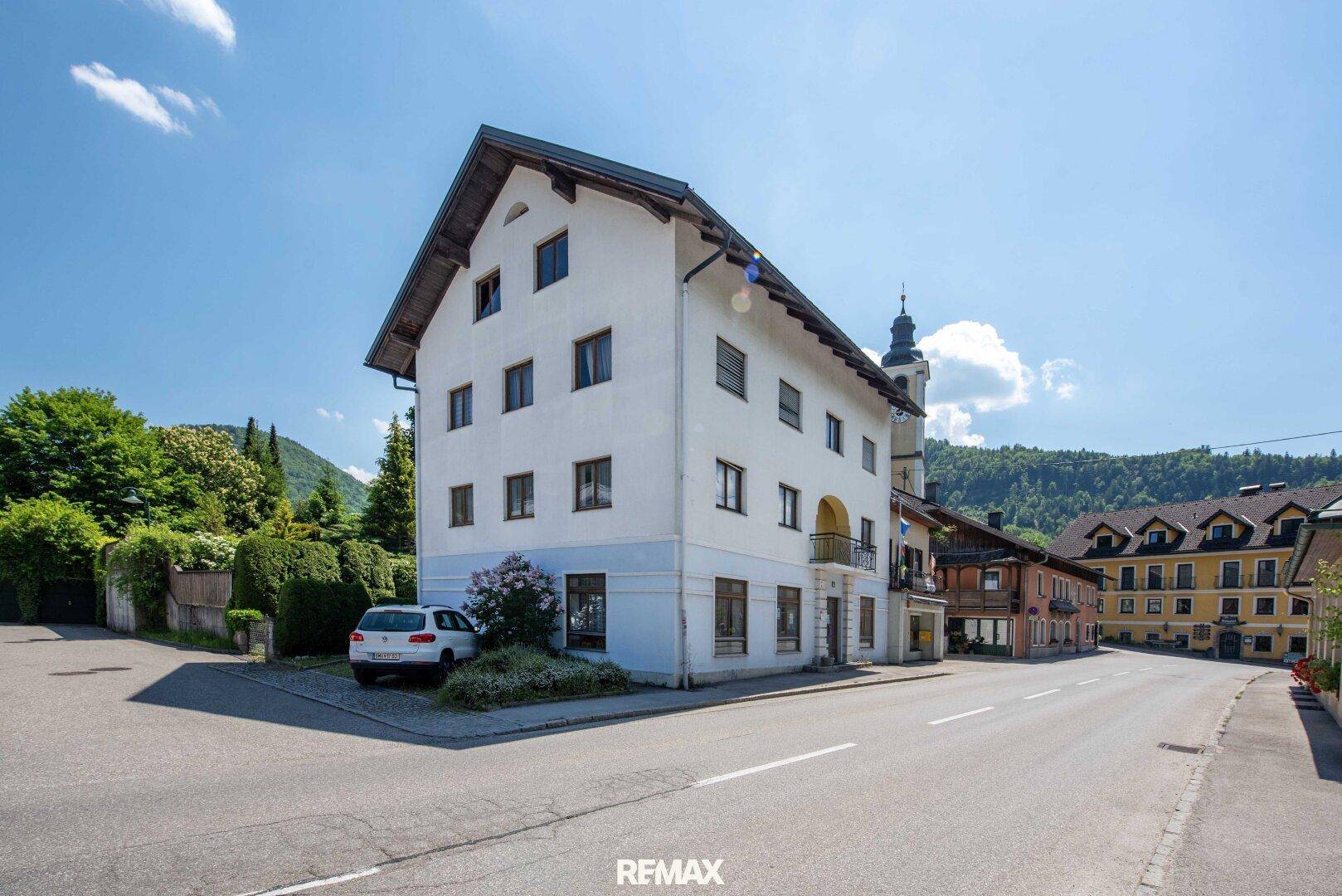 Weißes Mehrfamilienhaus mit Satteldach an einer Straße in ländlicher Umgebung.