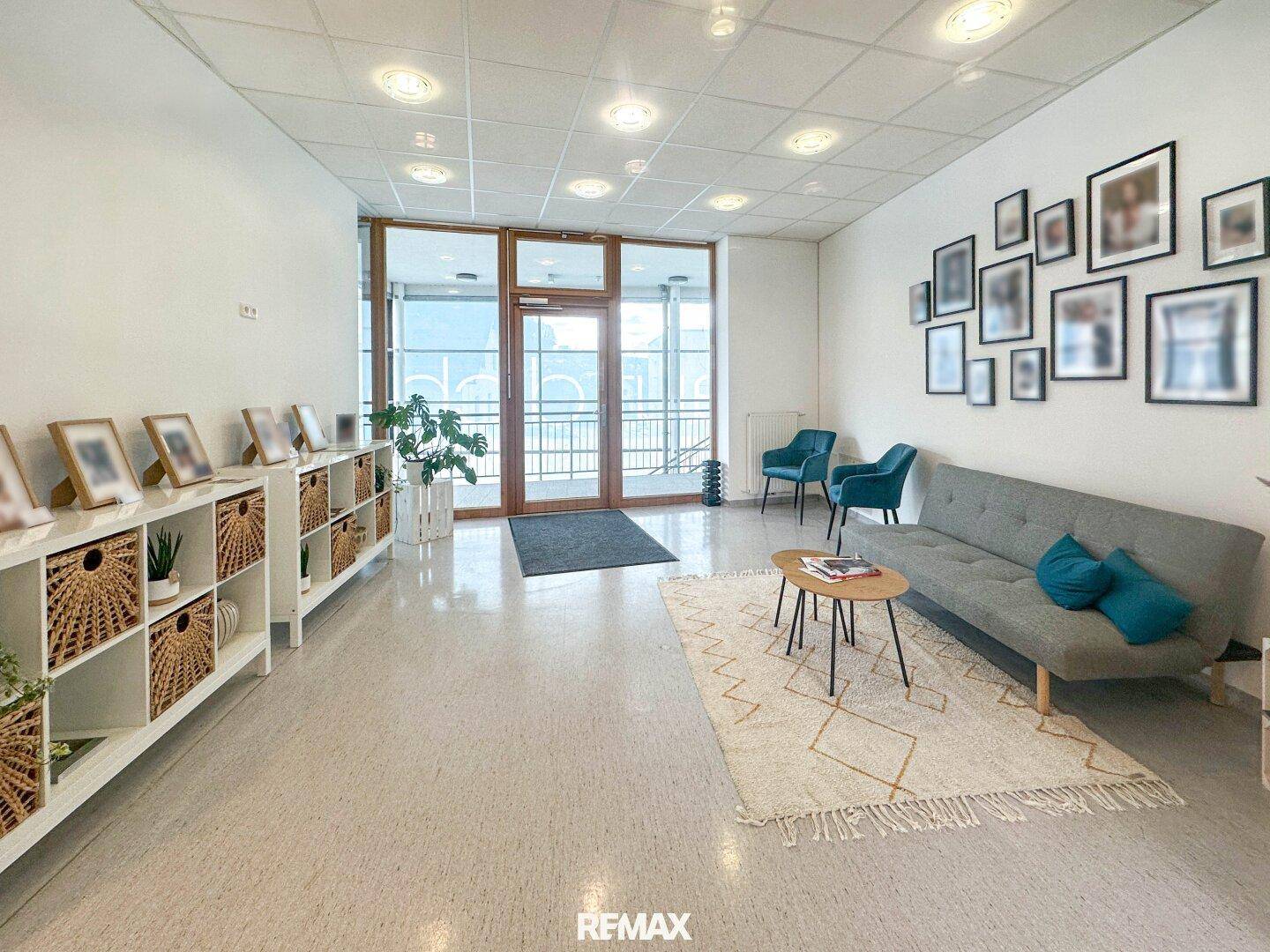 Heller Wartebereich mit bequemer Couch, Regalen und gerahmten Bildern an der Wand.