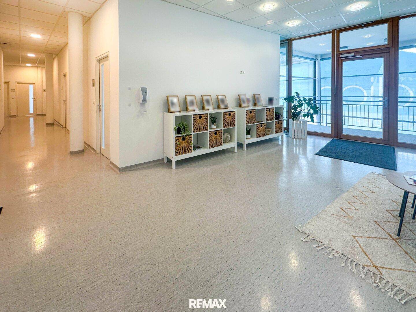 Heller Empfangsbereich mit langen Fluren, großen Glasfronten und dekorativen Regalen.