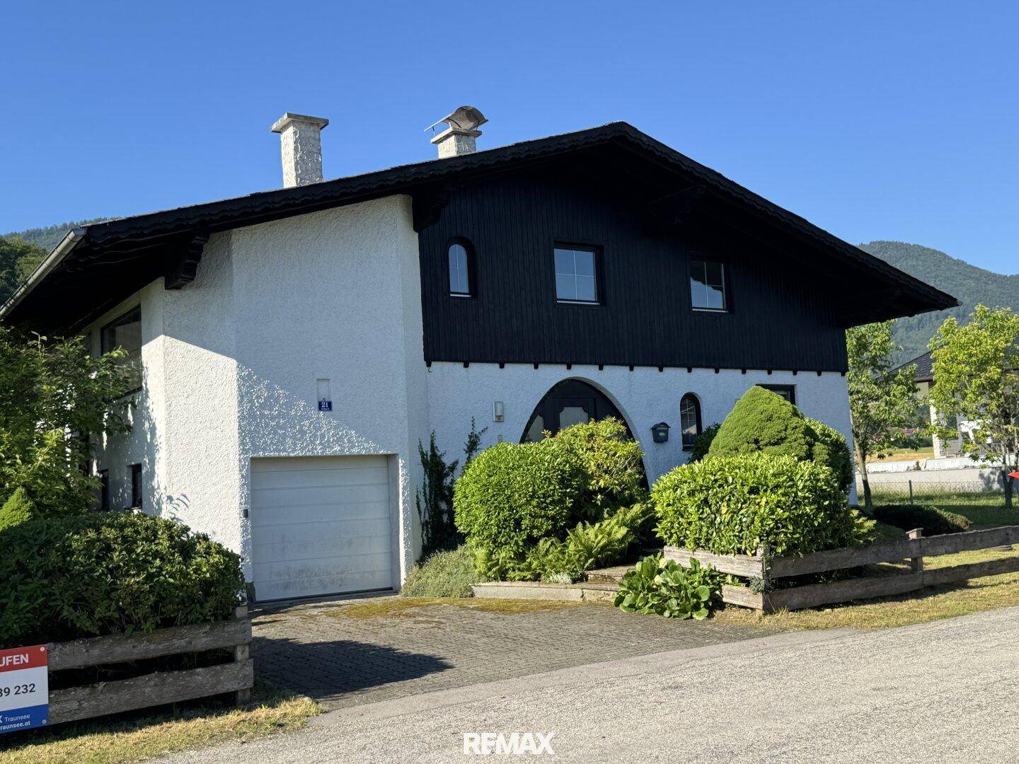 Vorderansicht eines traditionellen Hauses mit weißer Fassade, dunklem Holzbalkon und integrierter Garage.