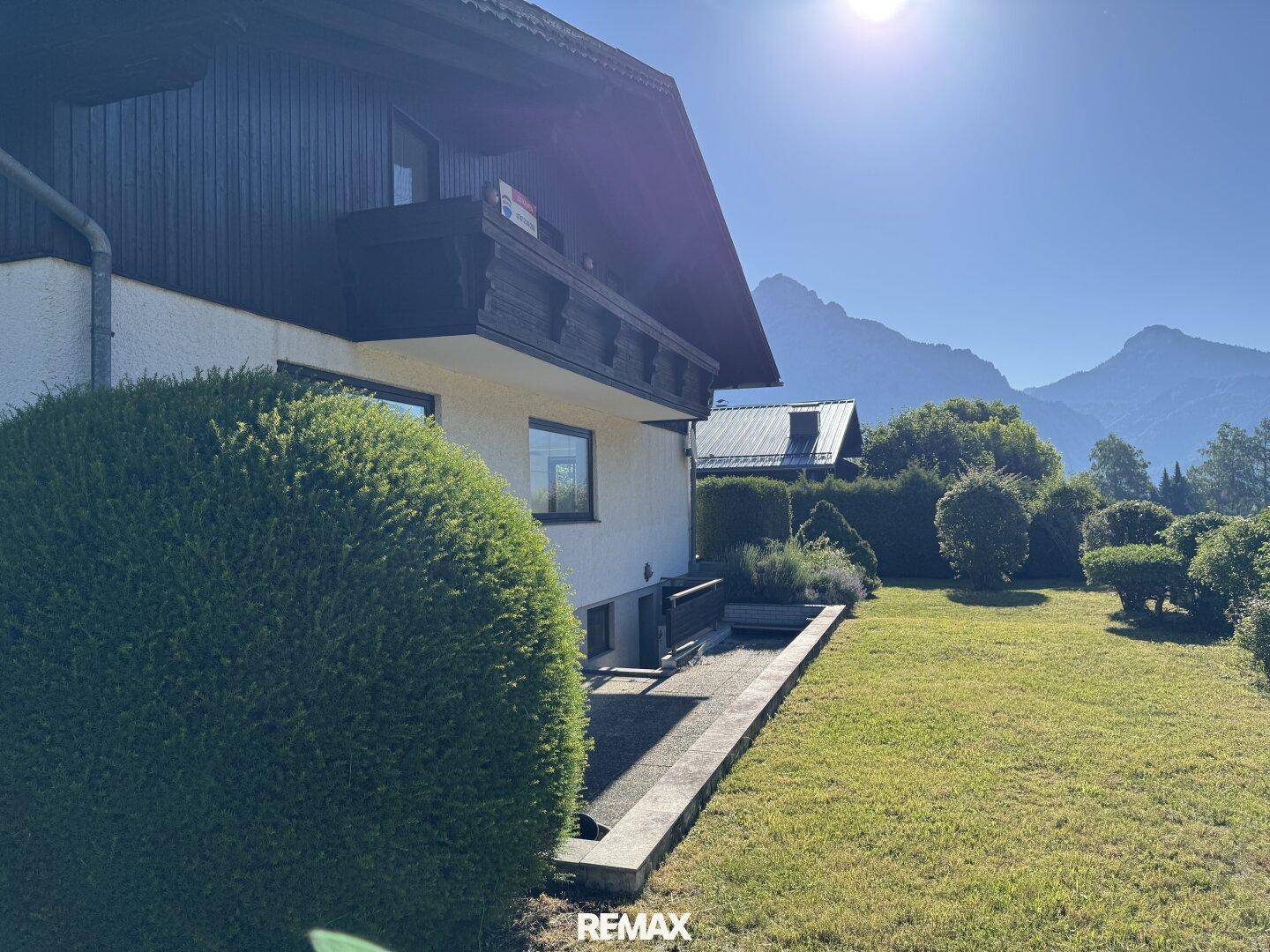 Seitlicher Blick auf das Haus mit gepflegtem Garten, Terrasse und Bergblick im Hintergrund.