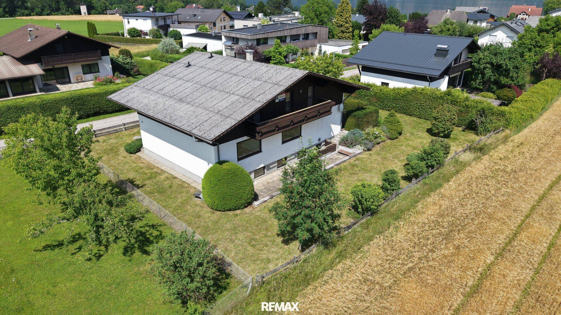 Luftaufnahme eines Einfamilienhauses mit Garten, umgeben von Feldern und anderen Häusern.
