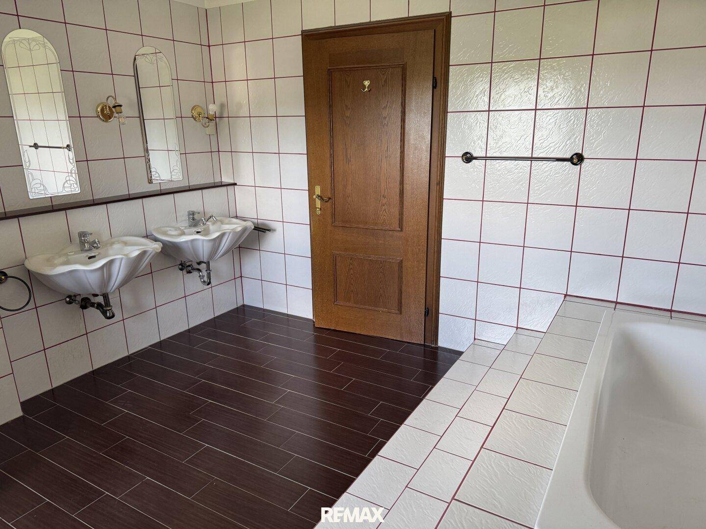 Badezimmer mit zwei Waschbecken, Badewanne und weißen Fliesen mit roten Akzenten.